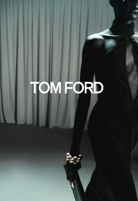 A fashion model in a black dress with gold jewelry is featured in a studio environment for a Tom Ford ad campaign.
