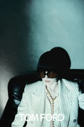 Model in oversized pinstripe blazer wearing dark sunglasses seated against a textured dark background for Tom Ford