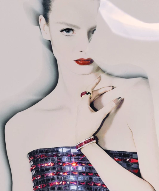 Close-up of a fair-skinned woman in a strapless jeweled top with red lips, wearing a matching bracelet and ring against a light background.
