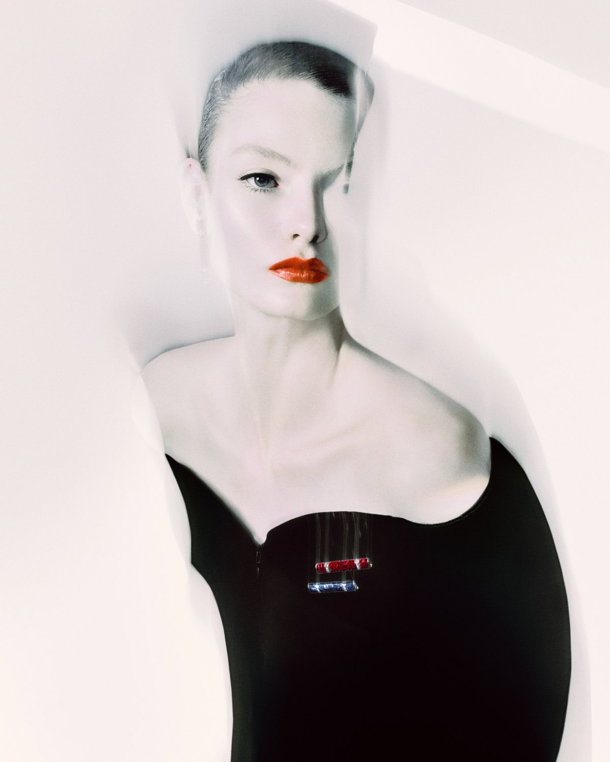 Close-up shot of a woman with short hair and red lipstick, wearing a black top against a bright white background in a fashion aesthetic.