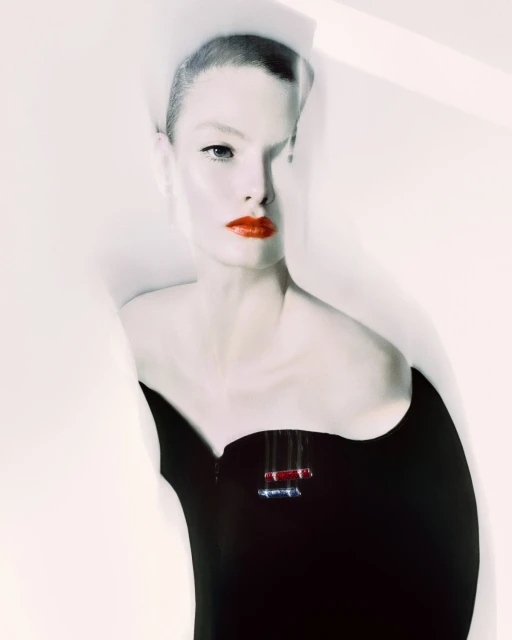 Close-up shot of a woman with short hair and red lipstick, wearing a black top against a bright white background in a fashion aesthetic.