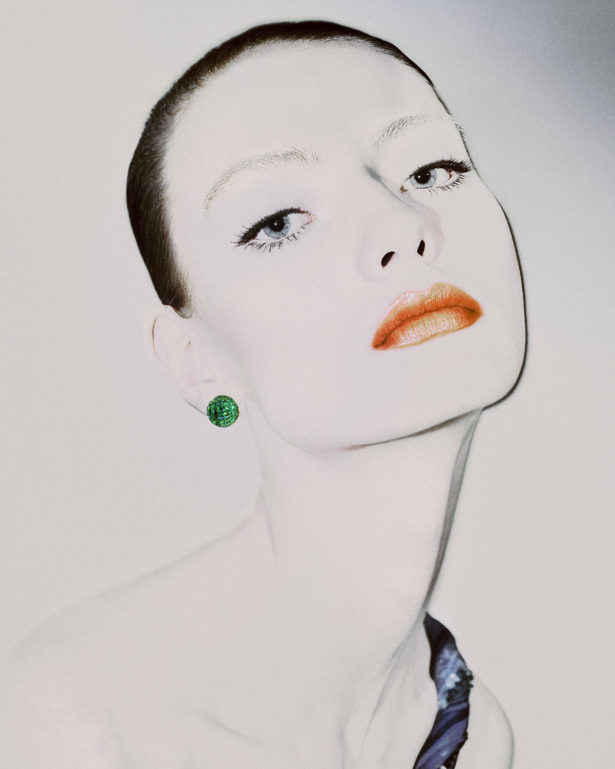 Artistic portrait of a stylish adult woman with green earrings looking up against a bright background in a beauty and fashion concept.
