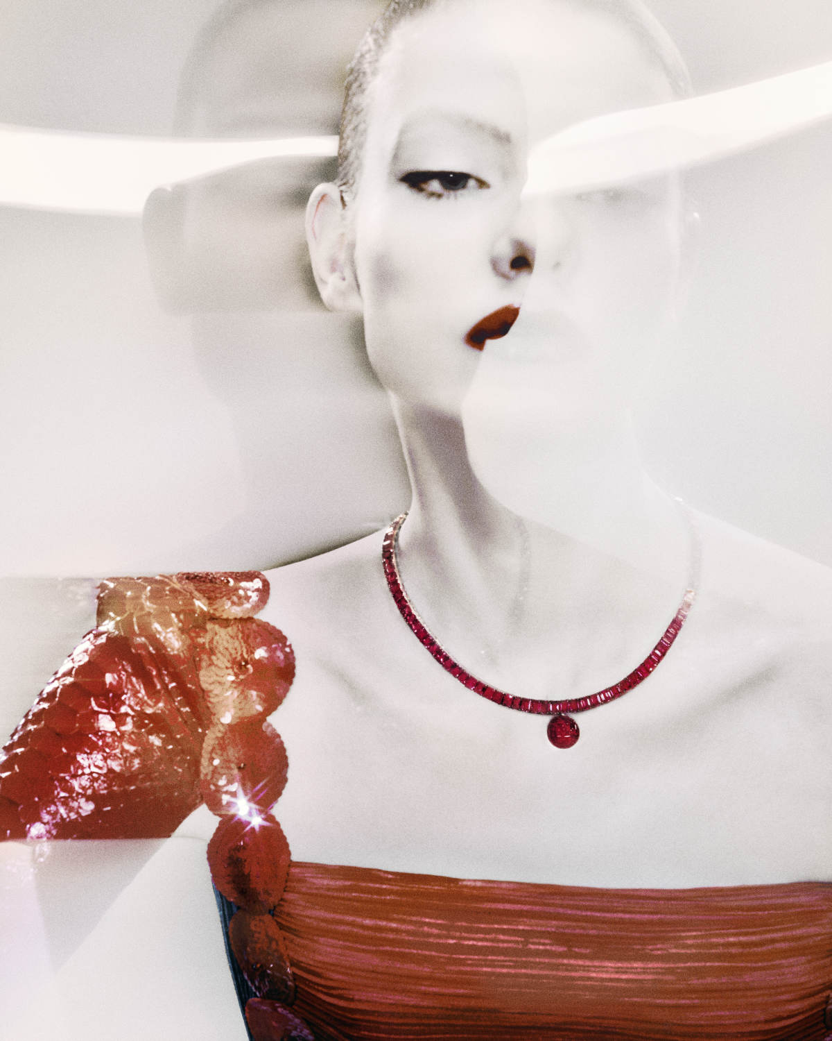 High fashion shot of a woman with a red lip wearing a red dress and matching necklace. The image has a light, airy quality.