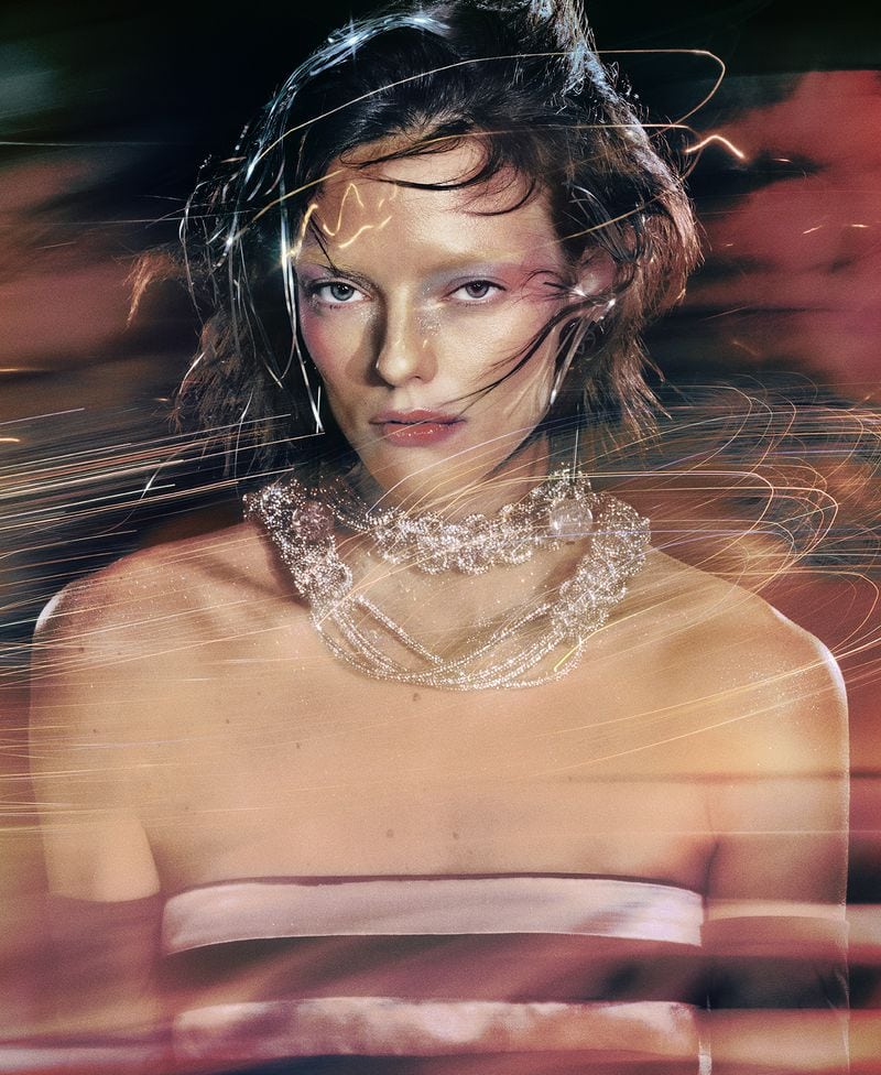 A young adult female model poses wearing a jeweled collar necklace, shot with long exposure light streaks in a blurred, vibrant background.