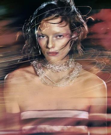 A young adult female model poses wearing a jeweled collar necklace, shot with long exposure light streaks in a blurred, vibrant background.