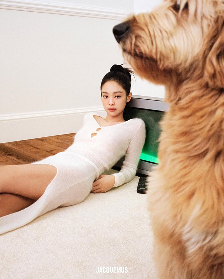 A woman in a white dress poses next to a TV and a golden doodle dog in an indoor setting, with the Jacquemus logo visible.