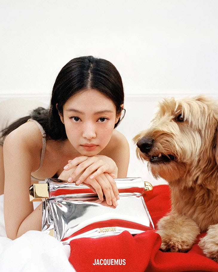 A woman poses with a metallic handbag and a dog indoors, featuring a red fabric accent and against a white backdrop.