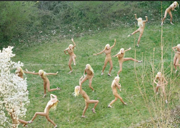 Aerial view of group of fair-skinned female adult dancers in tan bodysuits and blonde hair on a grassy lawn performing choreography.