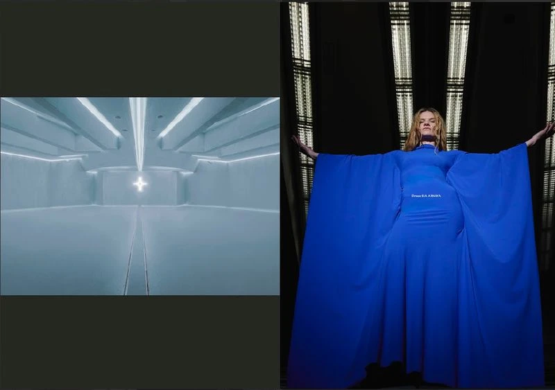 Adult female model in a blue dress with arms outstretched stands in front of a grid pattern in a studio with gray, cool tones.