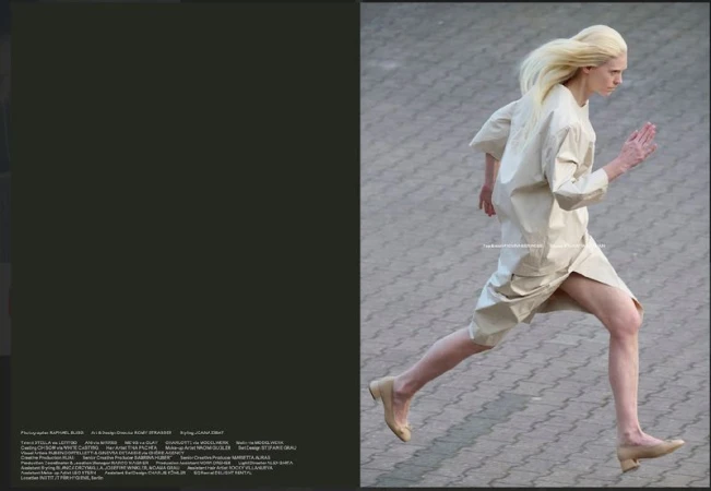 Fashion shot of androgynous fair-skinned adult running outdoors wearing beige tunic dress and beige ballet shoes on concrete surface.
