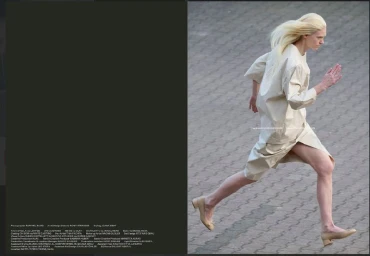 A blonde model wearing a cream-colored outfit running across a grey stone paved surface in a fashion editorial.