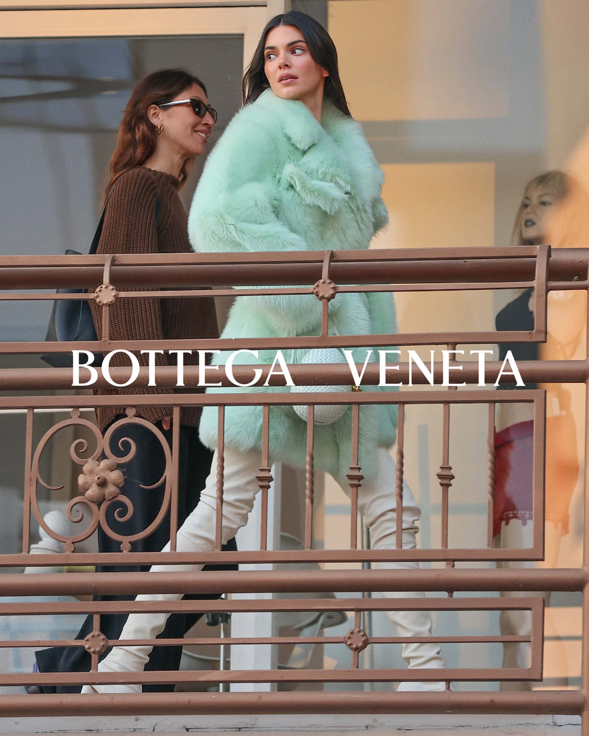 Kendall Jenner in a light green fur coat and white boots, walking on a balcony with other people, featuring Bottega Veneta text overlay.