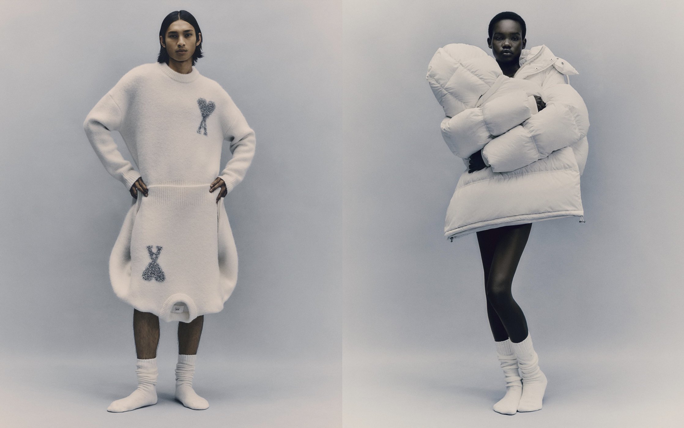 Two fashion models pose in a studio setting, showcasing oversized white knitwear and a large puffer jacket against a pale backdrop.