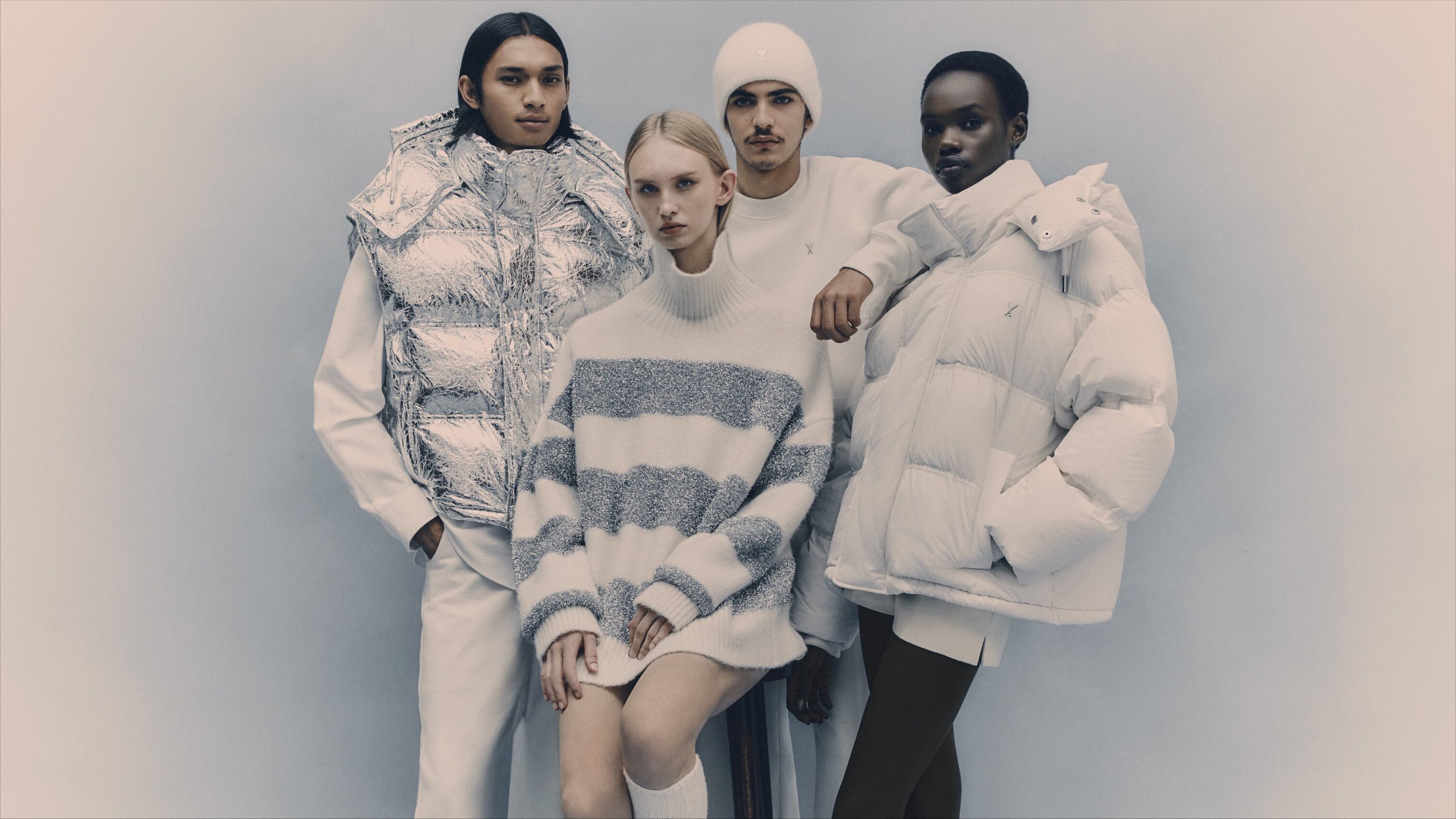 Four fashion models in white and grey winter clothing stand in front of a plain background, showcasing winter wear in a studio setting.