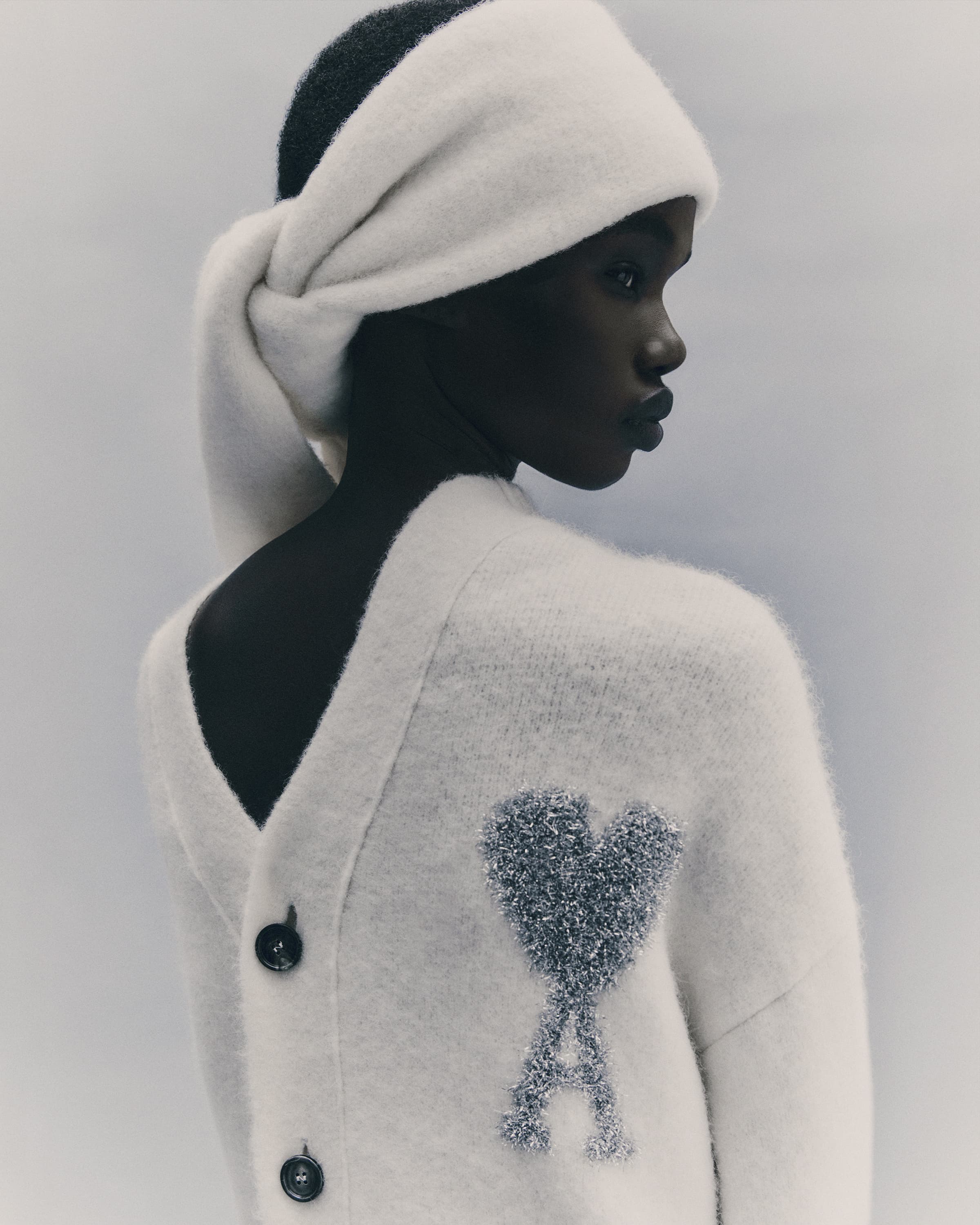 Model wearing a white cardigan backwards with a matching head wrap against a neutral studio background.