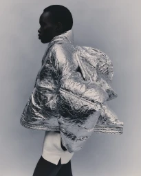 Model in a reflective silver puffer jacket and white skirt against a grey background