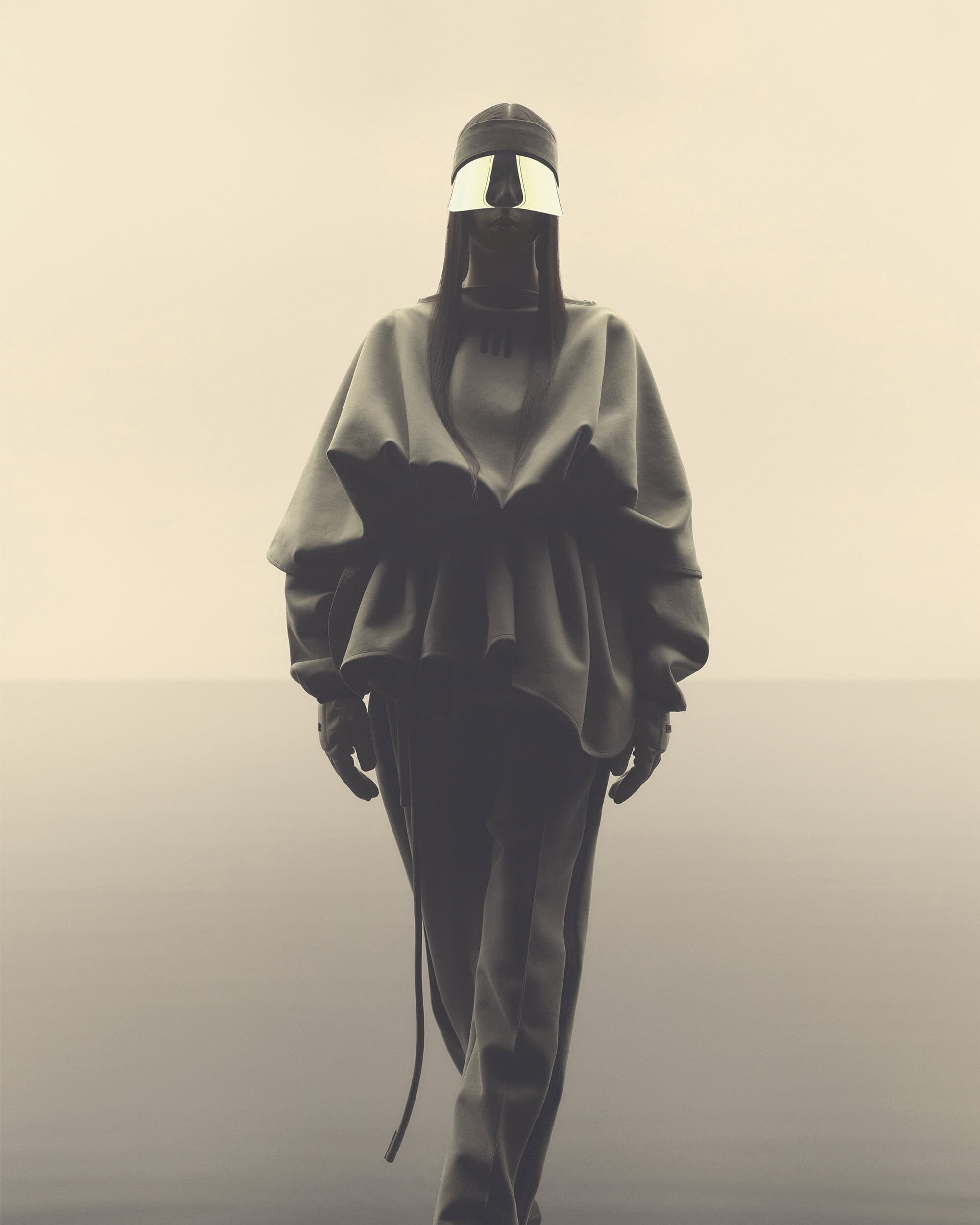 Monochrome fashion shot features a person wearing a sculptural garment with a reflective visor, standing against a neutral background.