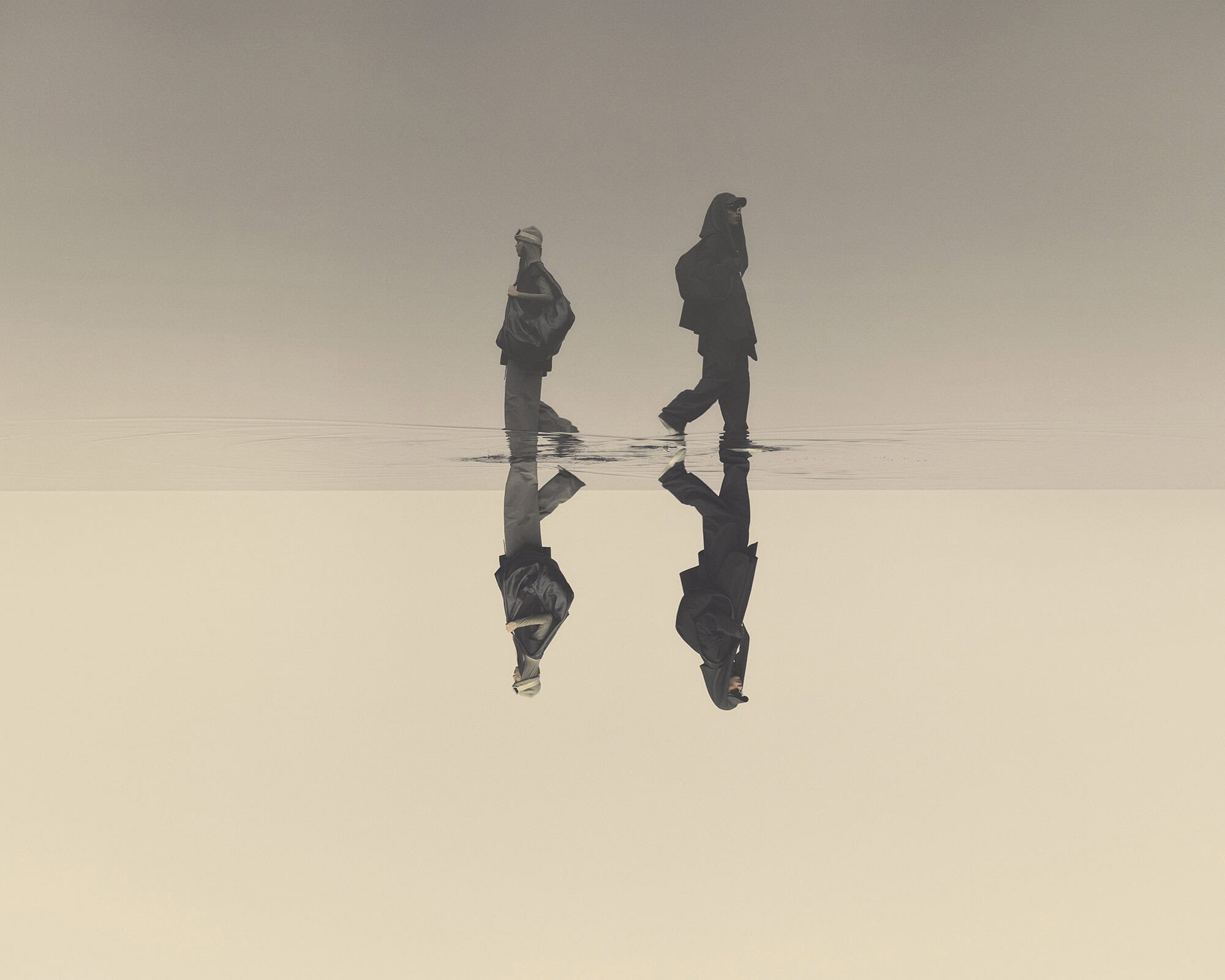 Two silhouetted figures wading through shallow water reflecting a light background, creating an ethereal, mirrored landscape.