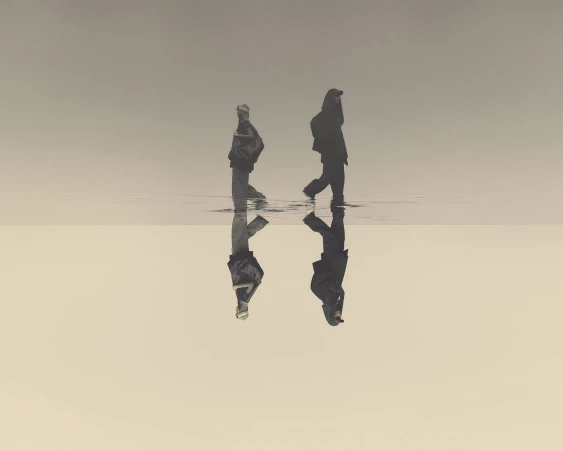 Two silhouetted figures wading through shallow water reflecting a light background, creating an ethereal, mirrored landscape.