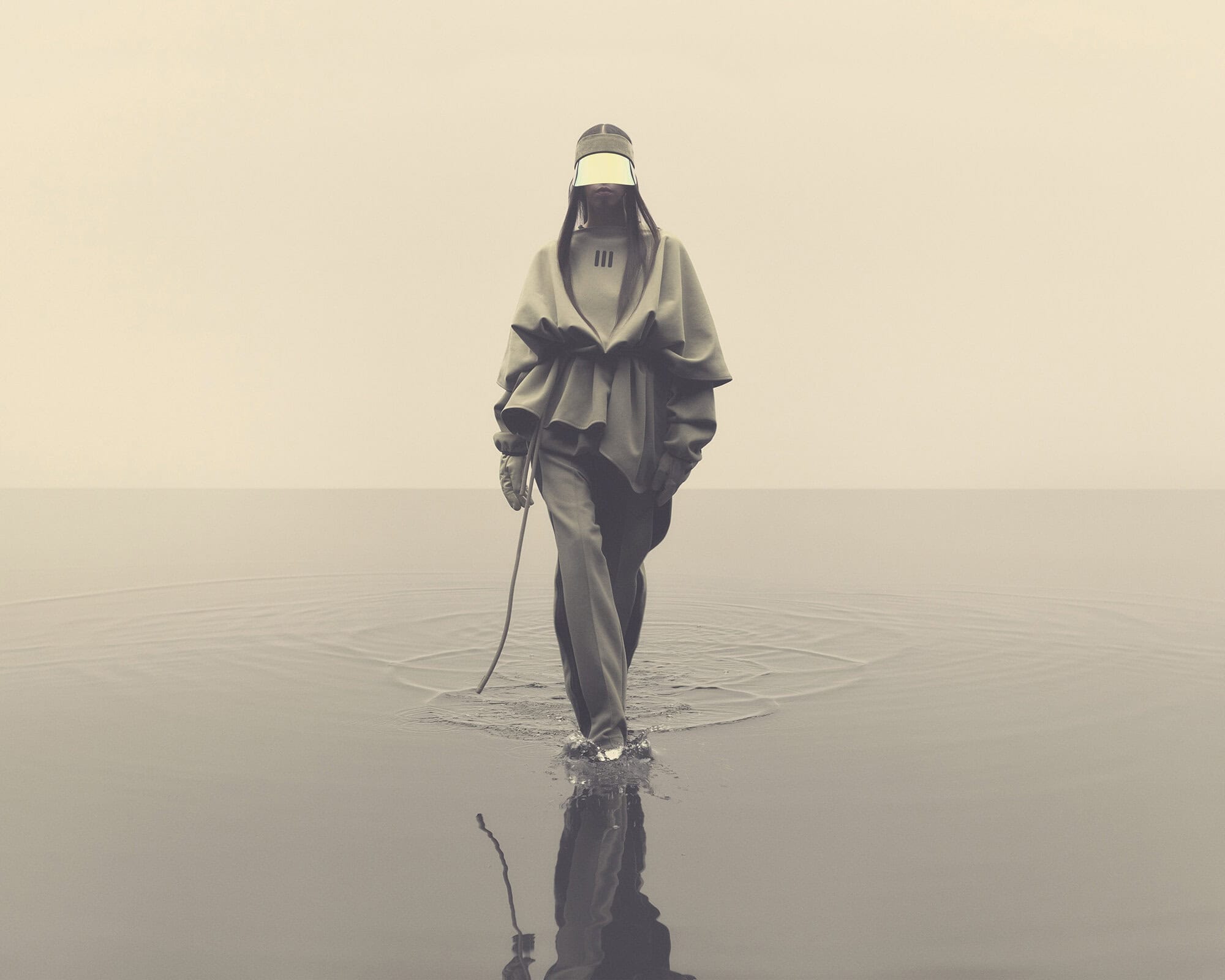 A lone woman in stylish grey outfit, wearing a visor, walks through a shallow body of water with a rope in hand on a foggy day.