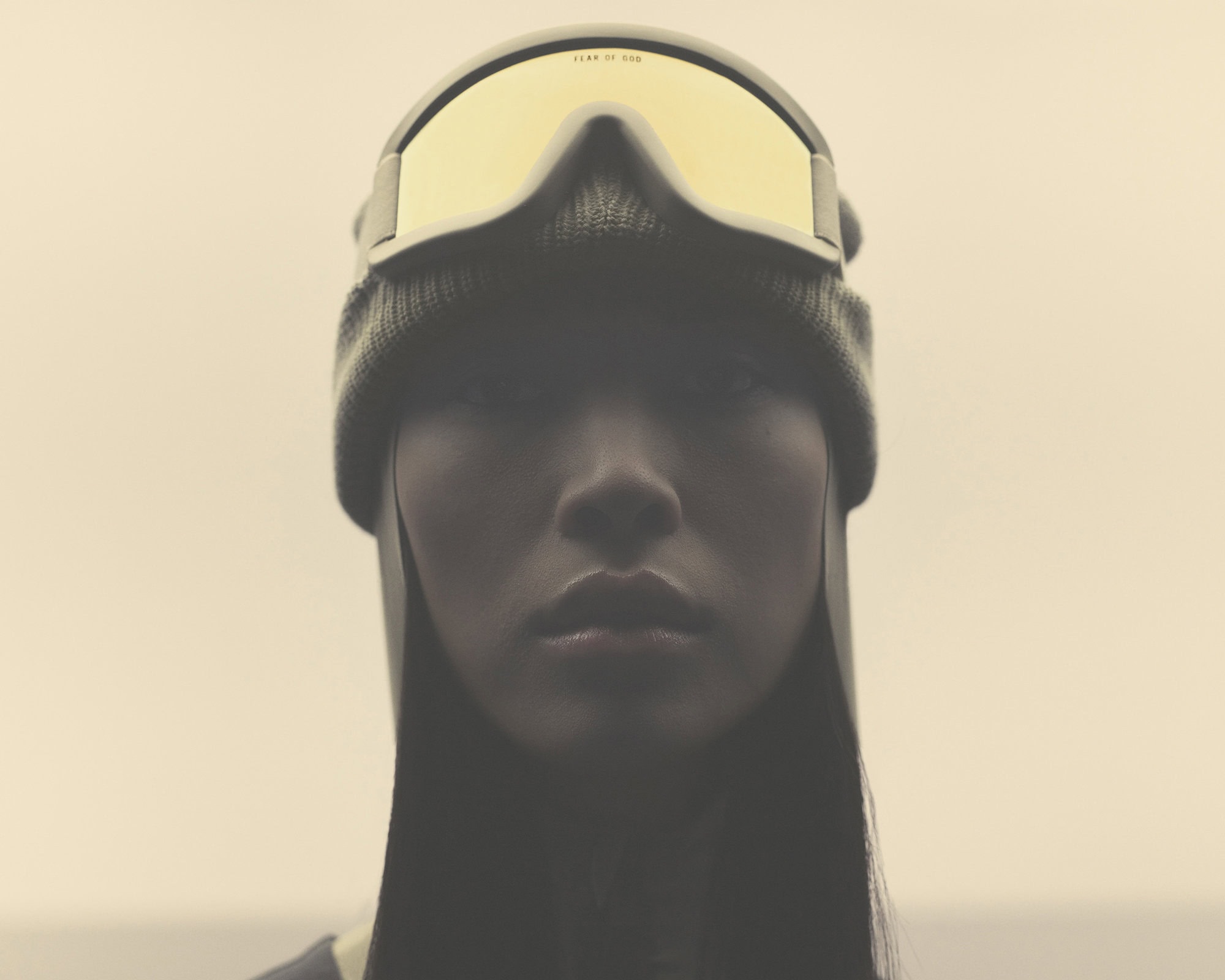 Portrait of an adult female wearing ski goggles and a knit cap against a neutral sky. She has straight black hair.