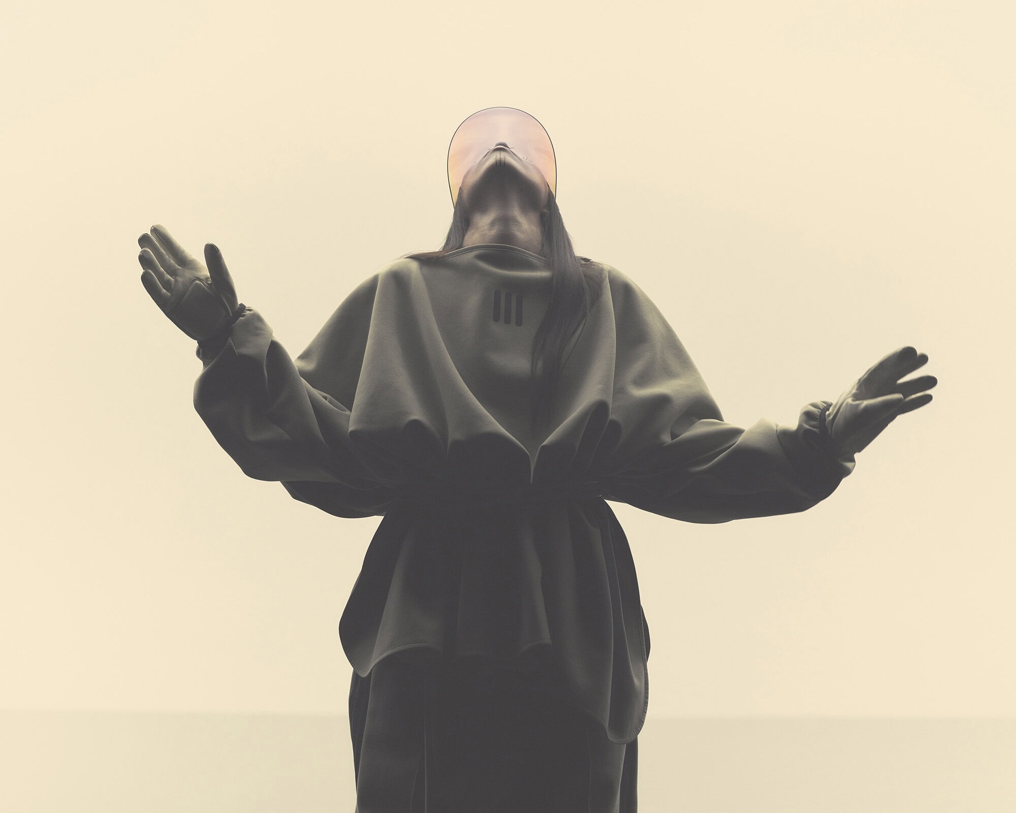 Abstract studio shot of a person in a hooded garment with arms raised, featuring an ethereal halo-like effect and soft lighting.