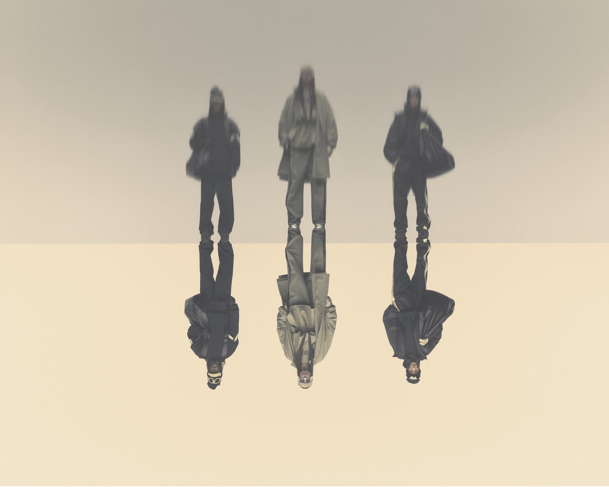 Three people stand in coordinated neutral-toned outfits with sharp reflections against a bright gradient backdrop in a fashion-forward editorial.