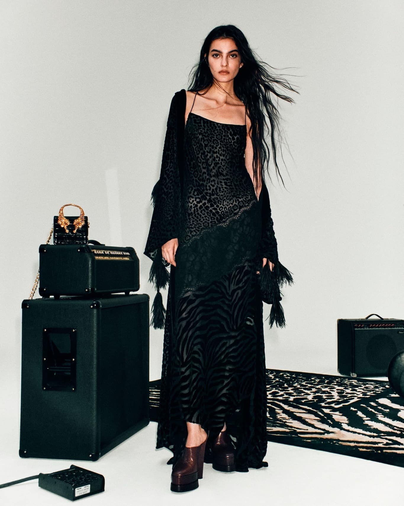 A woman poses in a black animal print dress, paired with brown platform heels, next to speakers and a matching black and brown rug.