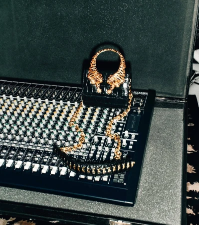 Close-up studio shot of a black purse with gold tiger heads on top of a sound mixing board inside of a black padded case.