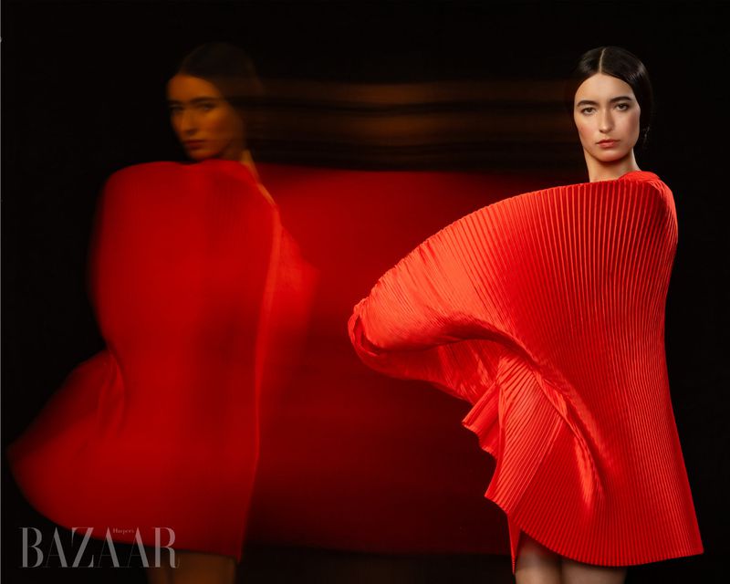 Fashion shot of a woman in a bright red, pleated, flowing dress against a dark background, soft studio lighting, beauty shot.