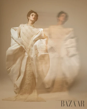 A woman is posing in a creamy white dress and jacket in a studio with motion blur and a creamy background, shot for Bazaar Magazine.