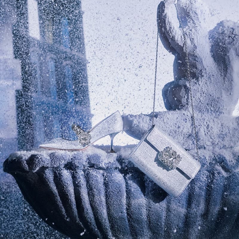 Elegant women's fashion: a sparkly silver stiletto heel and clutch purse with a crystal clasp sit atop a snow-covered fountain.