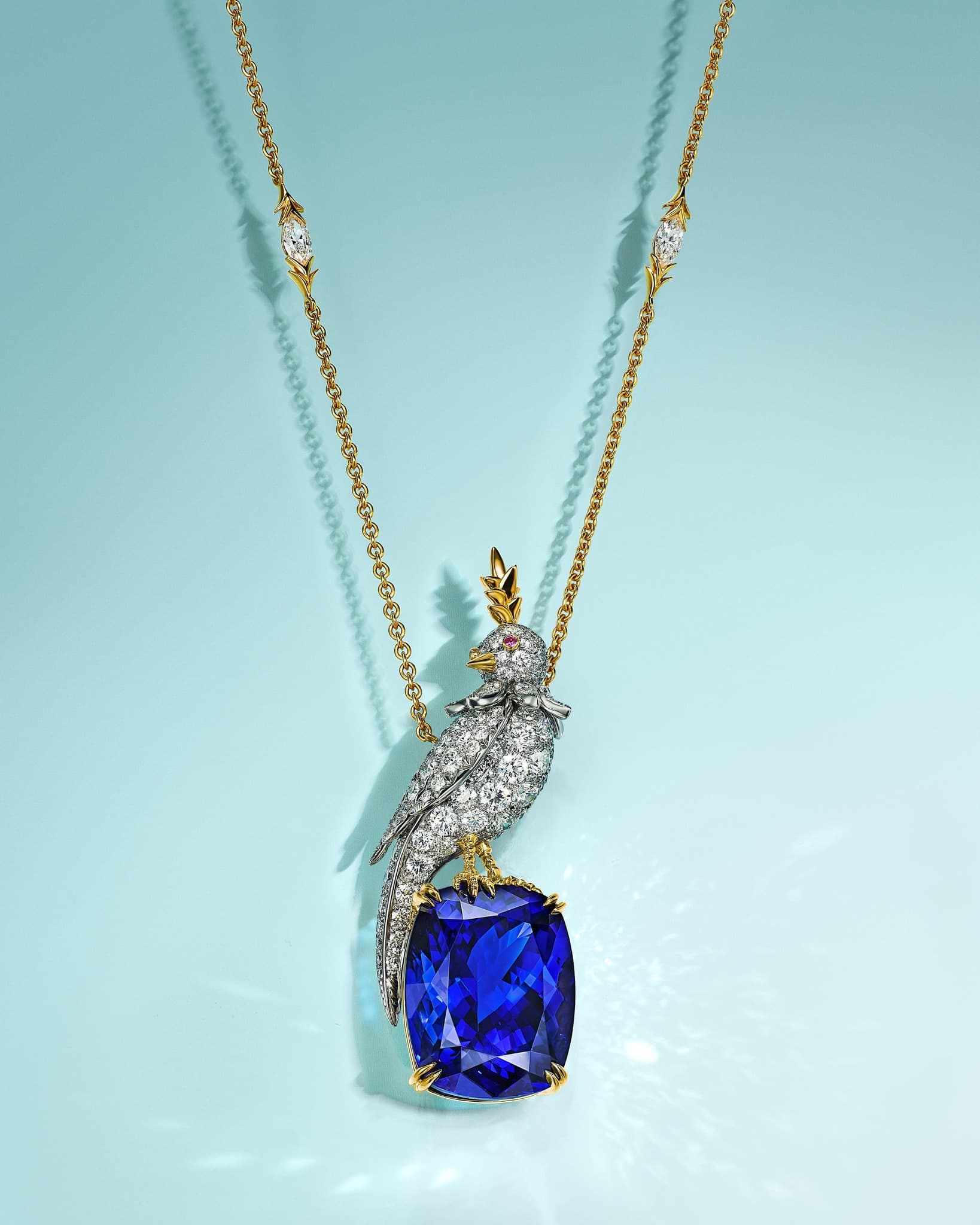 Necklace with an avian-shaped pendant encrusted with diamonds, perched atop a large, square-cut, deep-blue gemstone, against a light blue background.