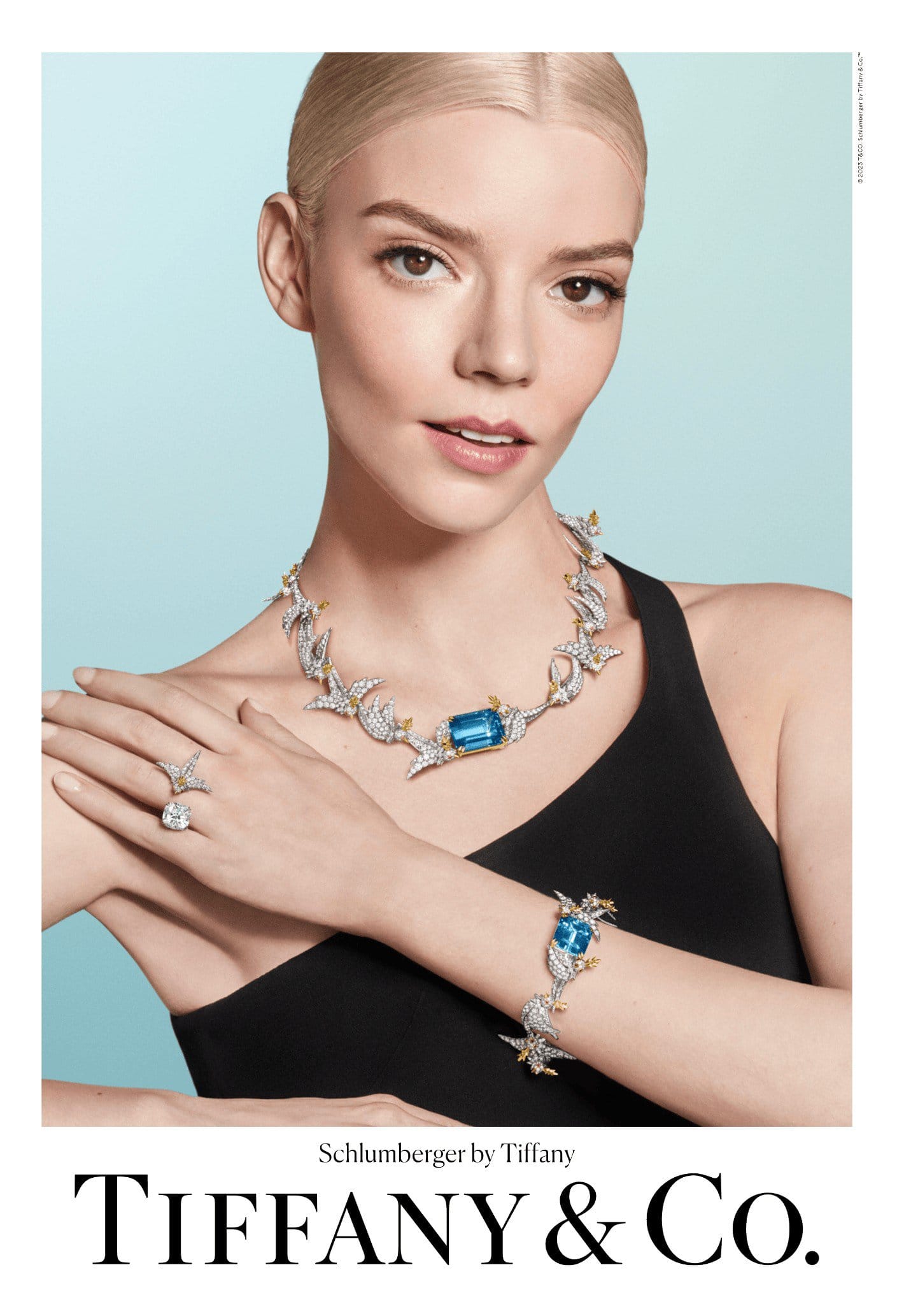 Anya Taylor-Joy wearing a diamond necklace, bracelet, and ring by Tiffany & Co. on a light blue background in a studio shot.