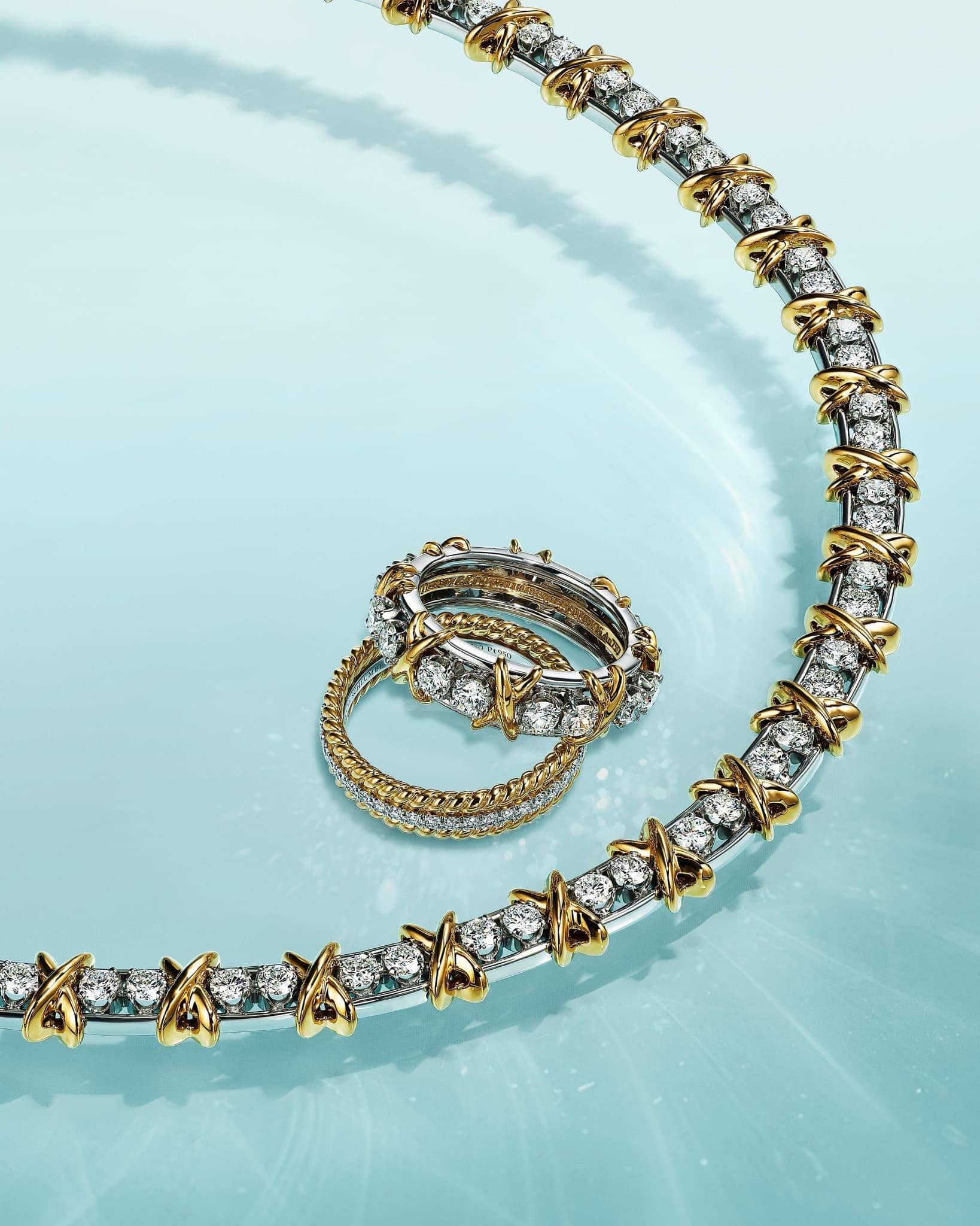 Elegant jewellery still life of a gold and silver gemstone encrusted necklace and rings on a light blue surface creating a luxurious look.