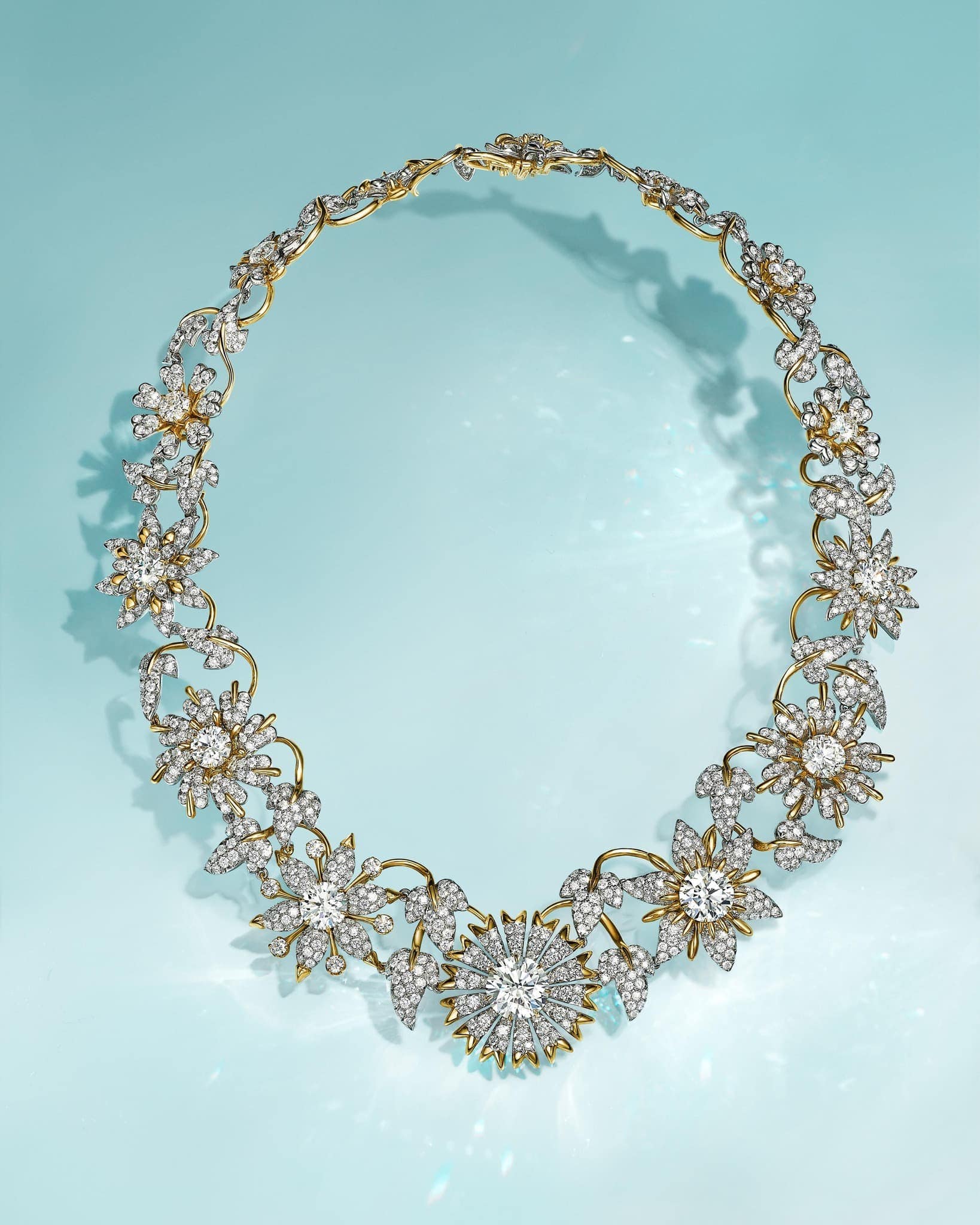 Elegant gold necklace with floral design and diamonds on a light blue background, jewelry, fashion, luxury, accessory, close-up.