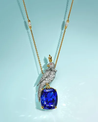 Diamond and gold bird pendant necklace resting on a large blue gemstone against a pale turquoise background