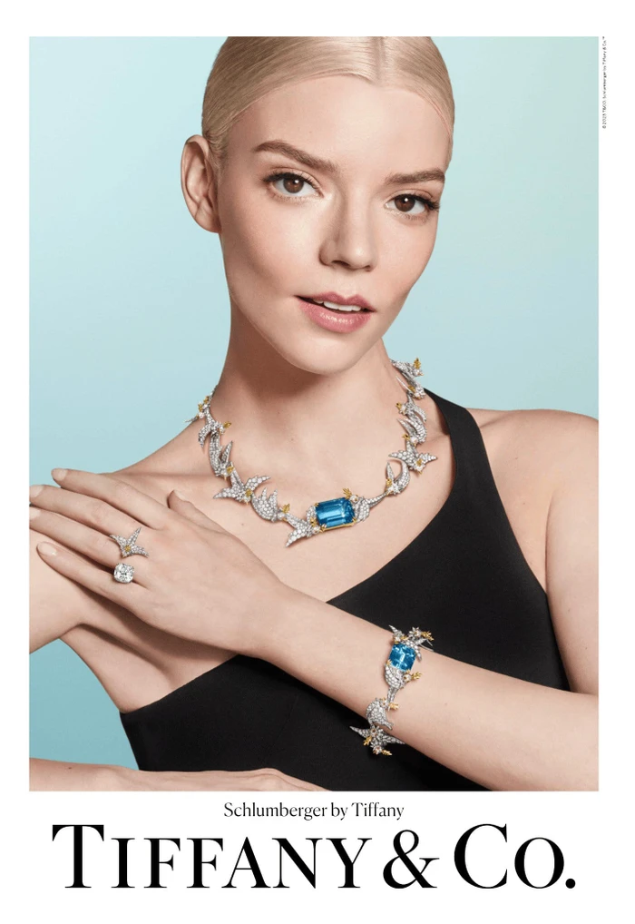 Anya Taylor-Joy wearing Tiffany & Co. diamond and aquamarine jewelry against a blue gradient backdrop.