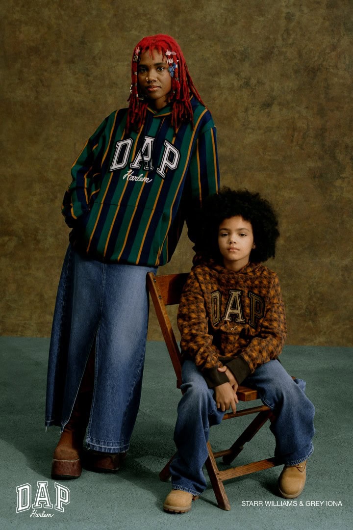 An adult and a child wearing Gap clothing are posing indoors against a mottled olive-green background, looking directly at the camera.