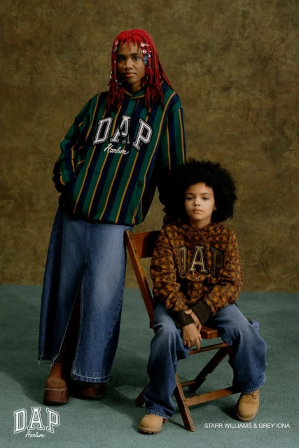 An adult and a child wearing Gap clothing are posing indoors against a mottled olive-green background, looking directly at the camera.