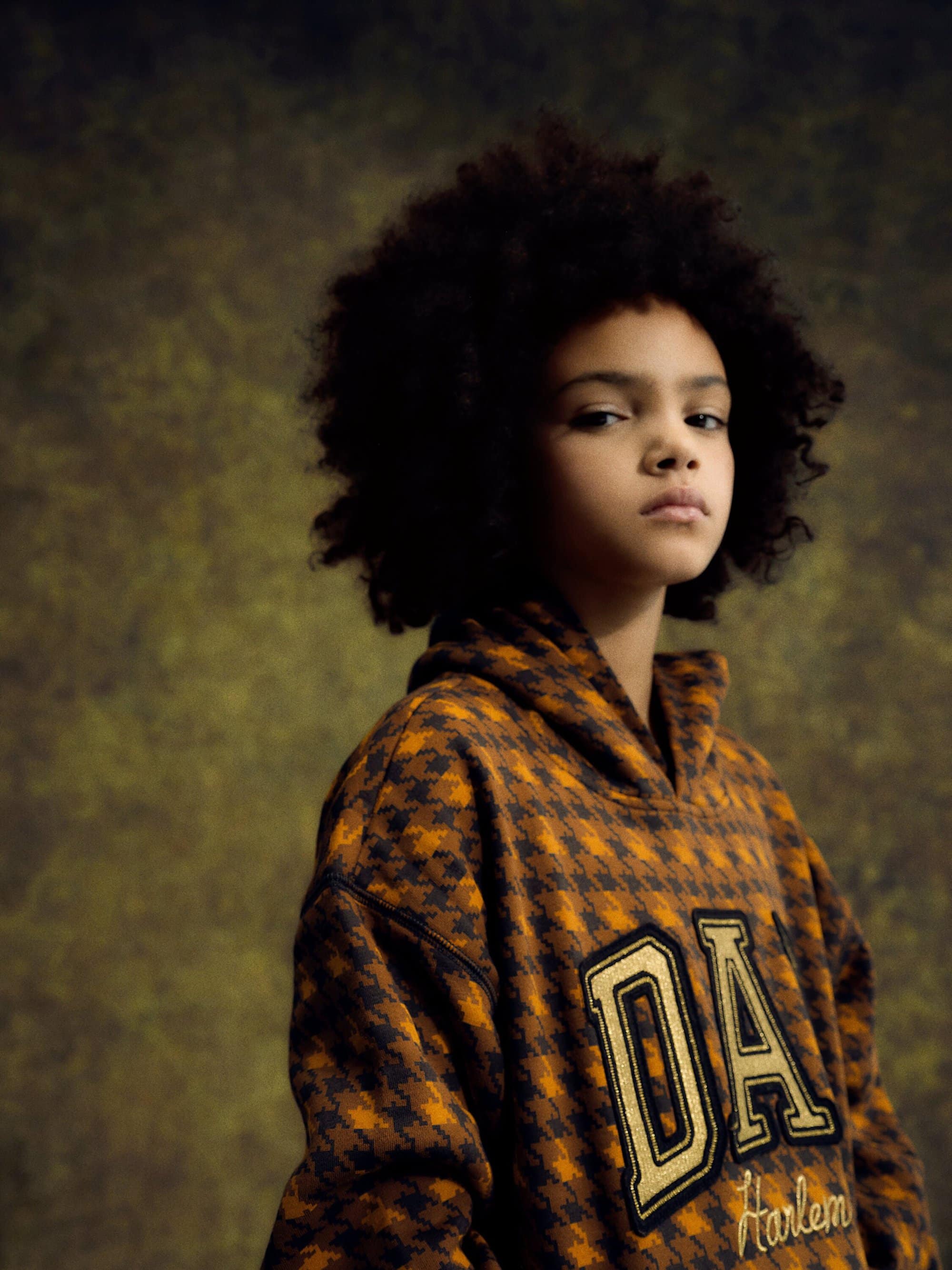 Portrait of a child with afro hair wearing a patterned hoodie. Studio background, natural lighting, fashion, and style.