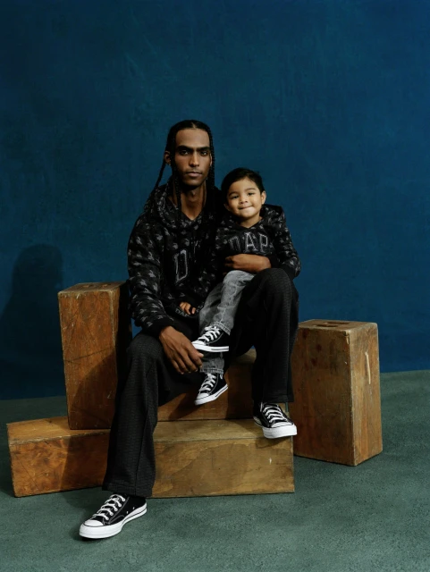 Adult and child sit together in an indoor studio setting wearing matching GAP hoodies and Converse sneakers; wooden blocks as props.