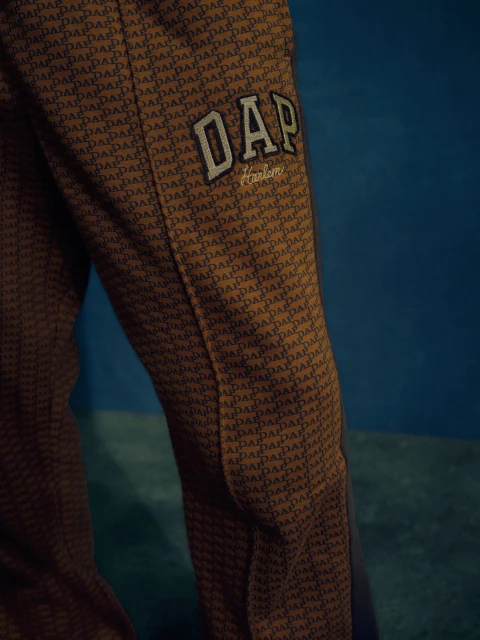 Close-up of patterned brown pants featuring the stitched 'DAP' logo in white against a dark blue background with side panel detailing.