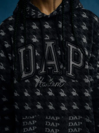 Close-up of a person wearing a black DAP hoodie with a houndstooth pattern and the word 'Harlem' embroidered.