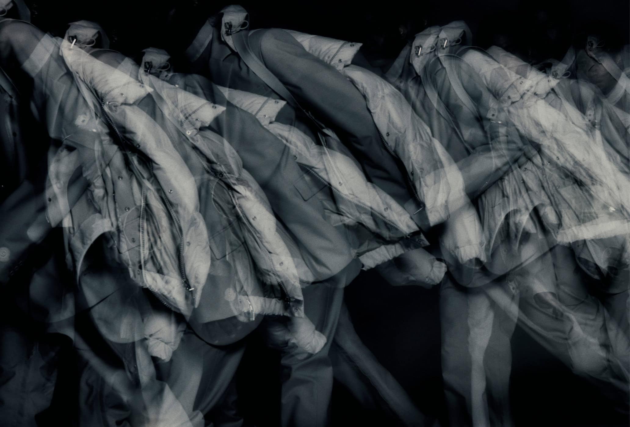 Abstract monochrome shot of multiple outwear jackets hanging, creating a sense of repetition and depth with blurry, overlapping outlines.