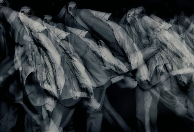 Abstract monochrome shot of multiple outwear jackets hanging, creating a sense of repetition and depth with blurry, overlapping outlines.
