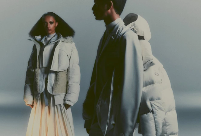 Two people model winter fashion, showcasing puffer jackets and stylish skirts in a studio setting with soft, diffused lighting.