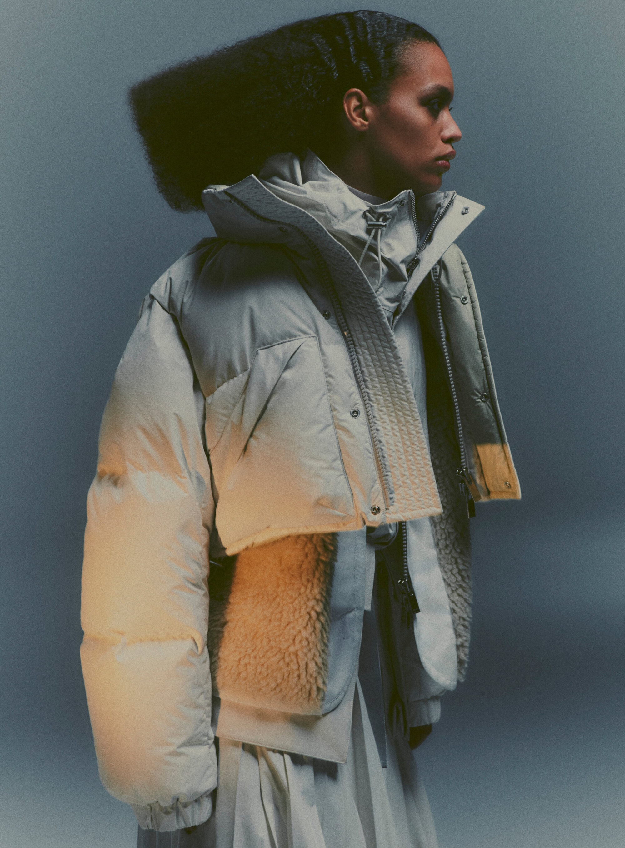 Fashion shot of a woman wearing a puffy winter jacket with asymmetrical design in a studio with soft lighting and neutral color grading.