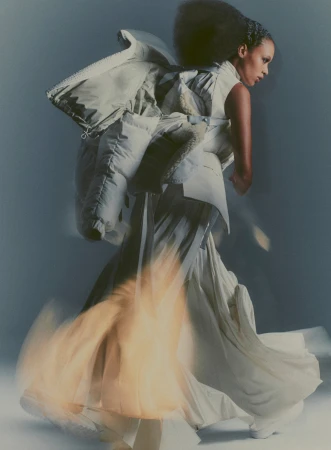 Fashion portrait of a woman with a dynamic pose wearing a futuristic, oversized white jacket and flowing skirt in a studio setting.