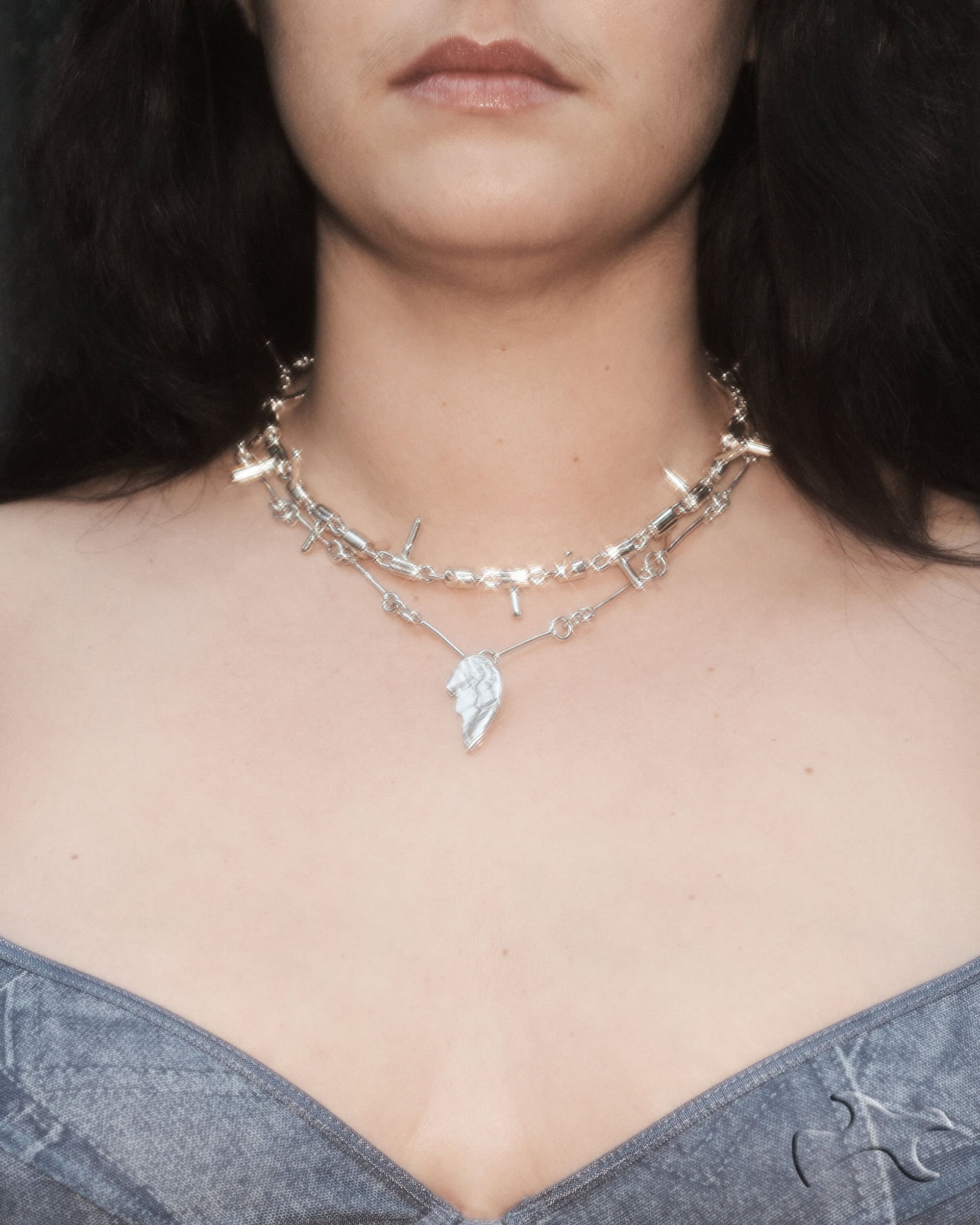 Close-up of a woman wearing a silver barbed wire choker necklace with a leaf pendant and a low-cut gray top. Beauty shot, fashion.